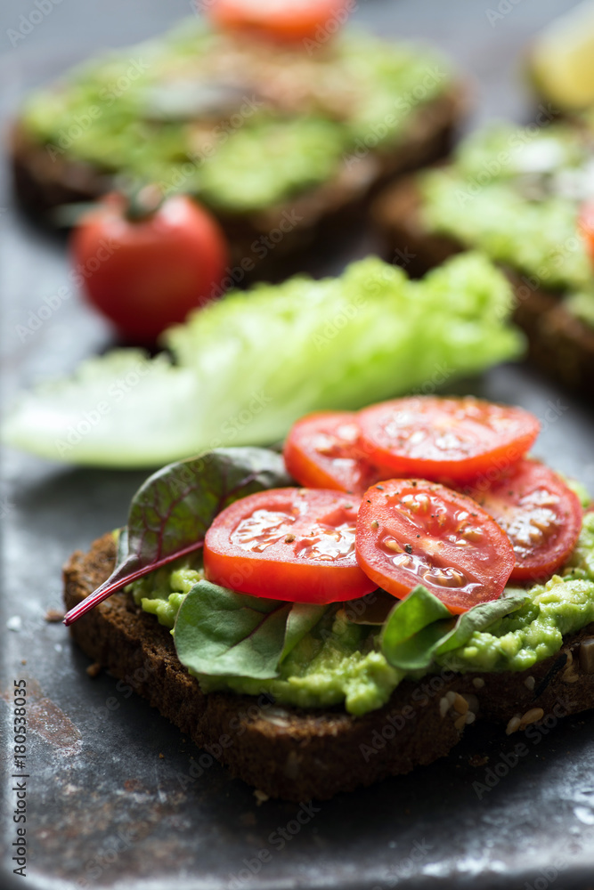 Toast with avocado, spinach and cherry tomato on whole grain rye bread. Closeup view, selective focus Toast with avocado, spinach and cherry tomato on whole grain rye bread. Closeup view, selective focus