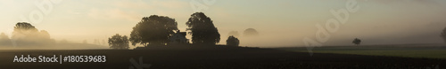 A very special panorama picture  mystic and eventful with trees and fog hanging over a farm building in the center of the panorama.       