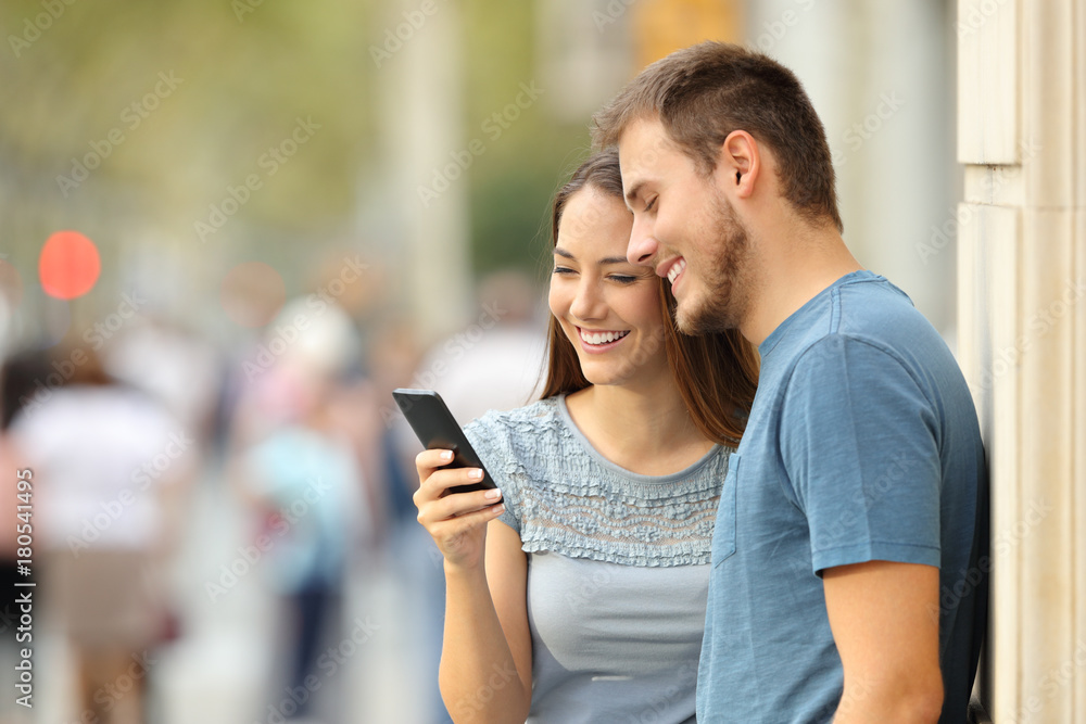 Couple watching on line media in a smart phone on the street Couple watching on line media in a smart phone on the street