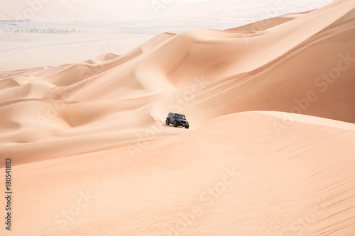 Fototapeta Naklejka Na Ścianę i Meble -  A single black car scaling giant sand dunes in the Empty Quarter desert. Abu Dhabi, UAE.