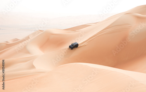 A single black car scaling giant sand dunes in the Empty Quarter desert. Abu Dhabi, UAE.