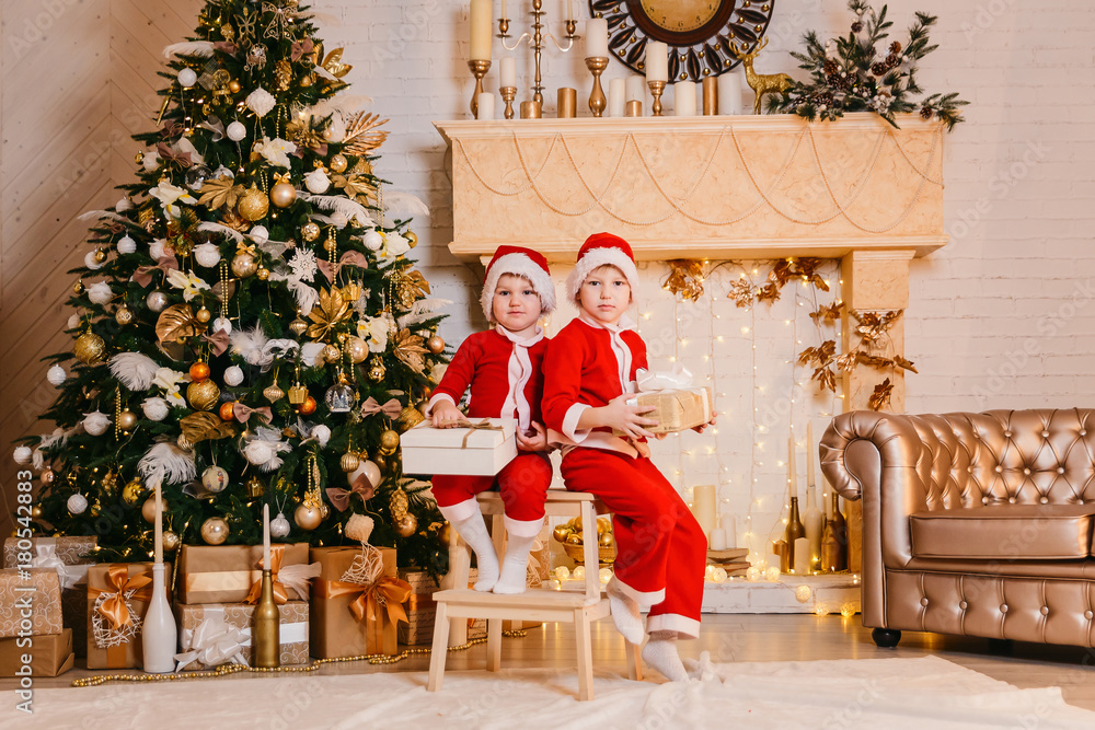two boys in Santa costumes are sitting under the tree