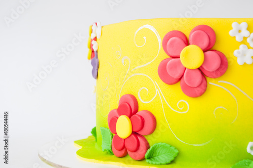 Fototapeta Naklejka Na Ścianę i Meble -  Colorful children's birthday cake made of yellow mastic decorated with pink flowers, leaves, pattern on a white background. Close-up. Cutout. Picture for a menu or a confectionery catalog.