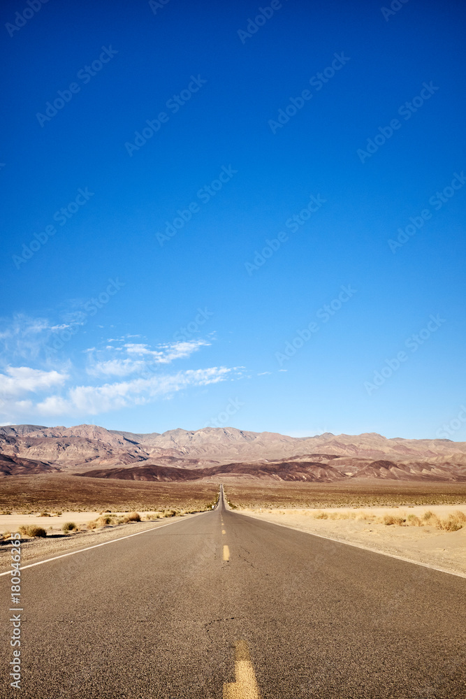 Empty straight road leading to mountains in Death Valley, California, USA