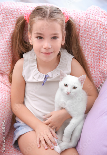 Little girl sitting in armchair with white cat indoors