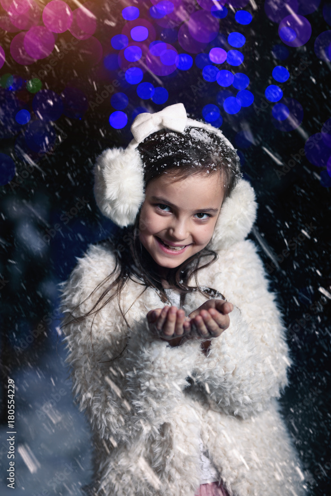 Fototapeta premium Young girl blows snowflakes in winter evening