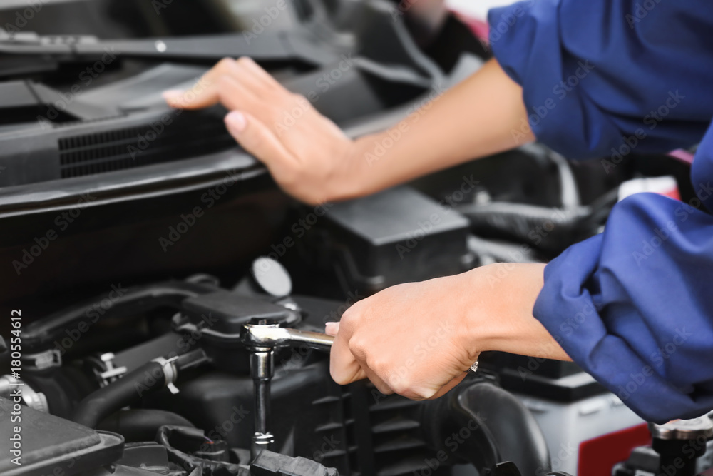 Young female mechanic repairing car in body shop