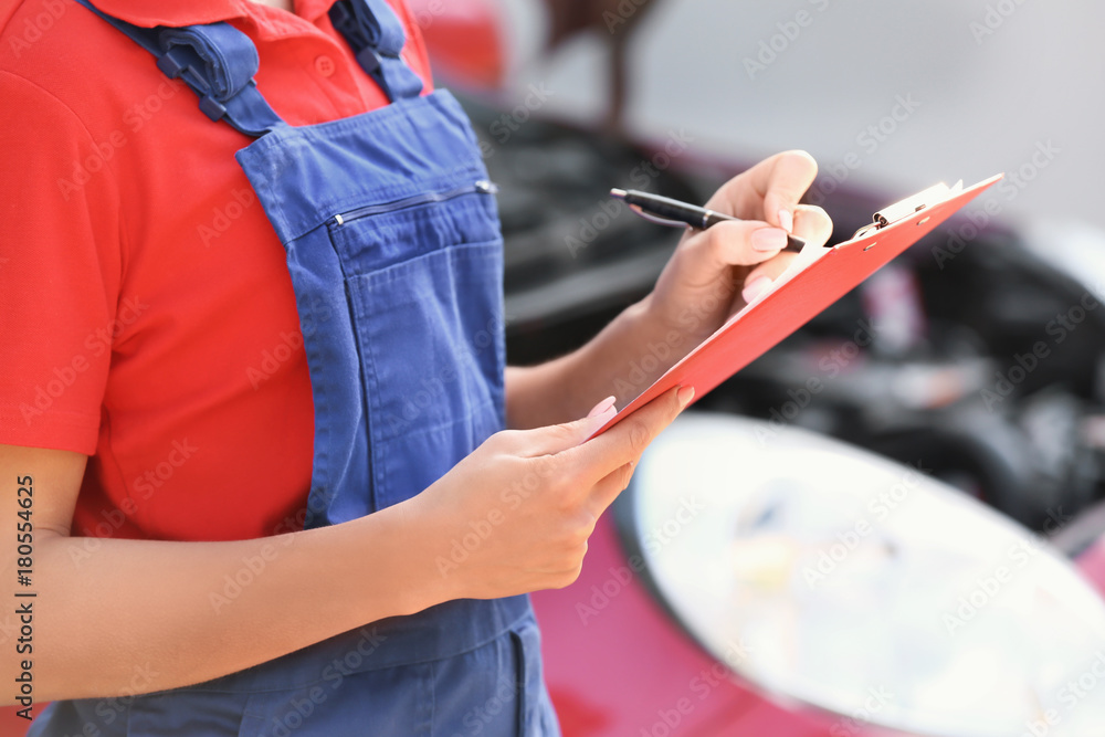 Obraz premium Young female mechanic with clipboard near car outdoors