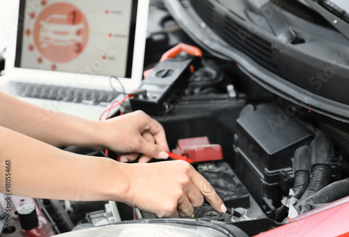 Young female mechanic with laptop repairing car in body shop