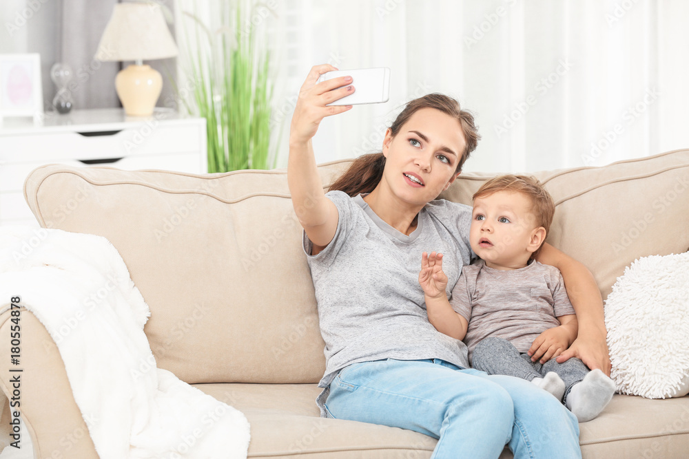 Mother with baby boy taking selfie on sofa at home