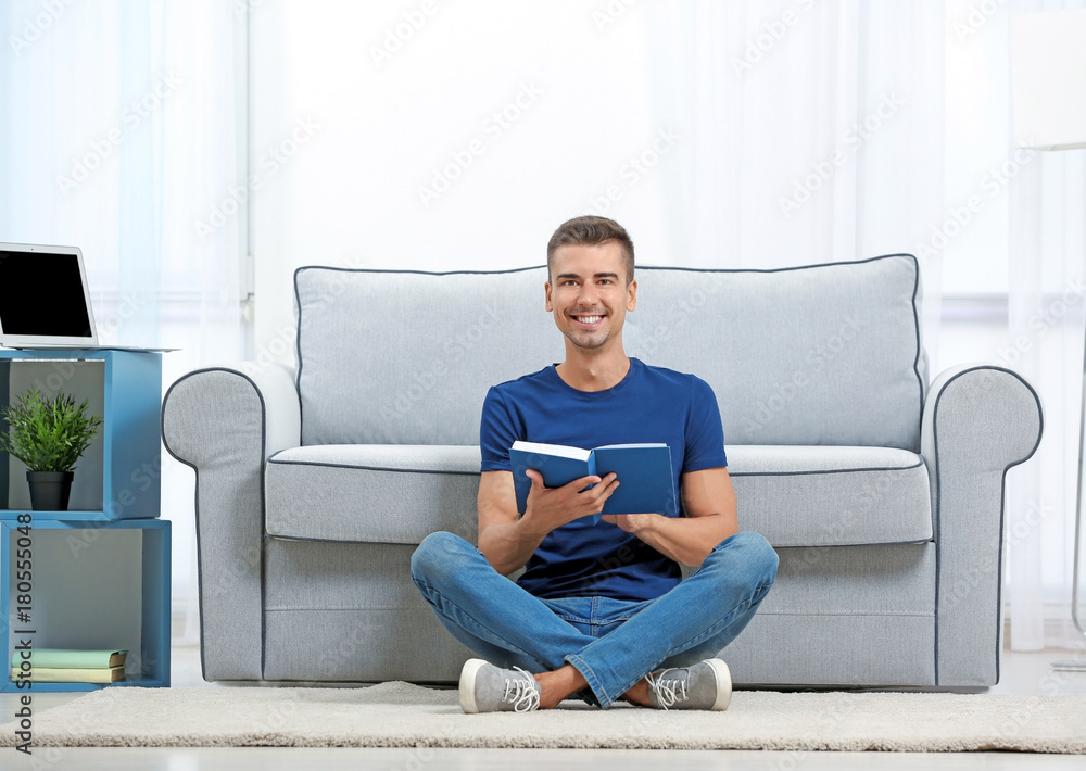 Young man reading book near sofa at home