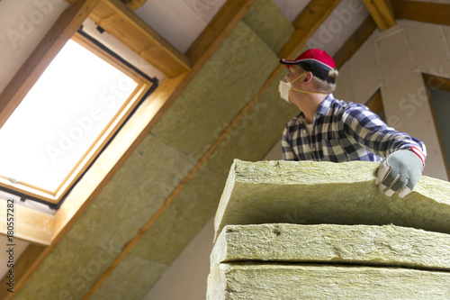 Man installing thermal roof insulation layer  - using mineral wool panels. Attic renovation and insulation concept