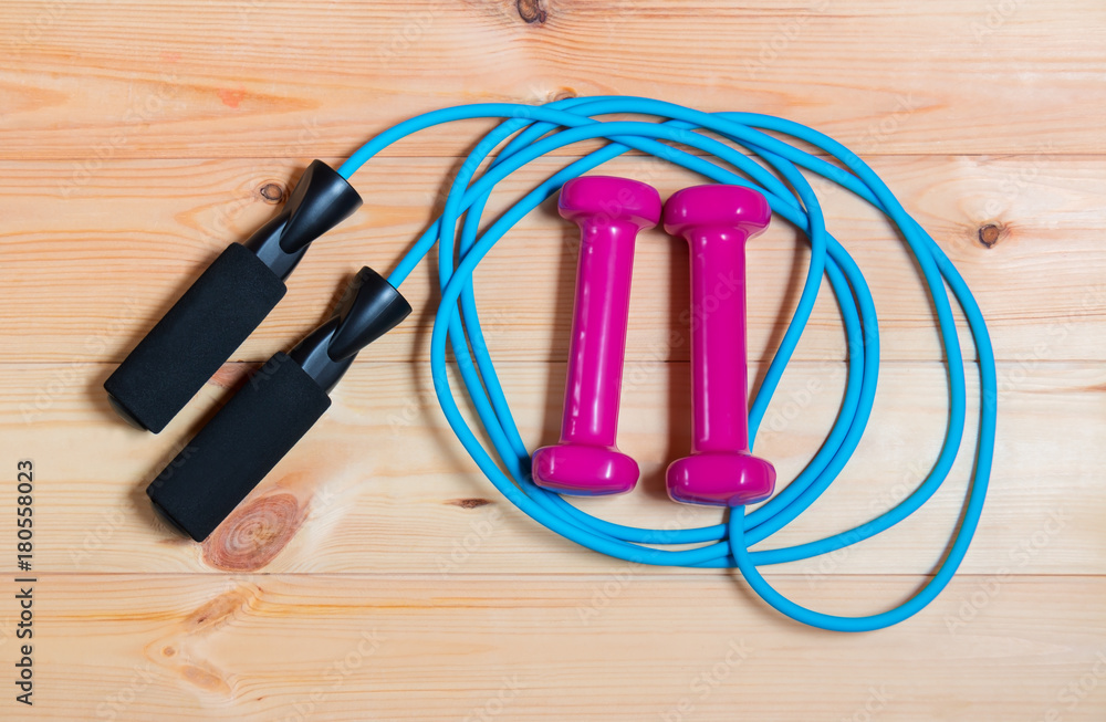 Dumbbells and skipping rope on wooden background Dumbbells and skipping rope on wooden background