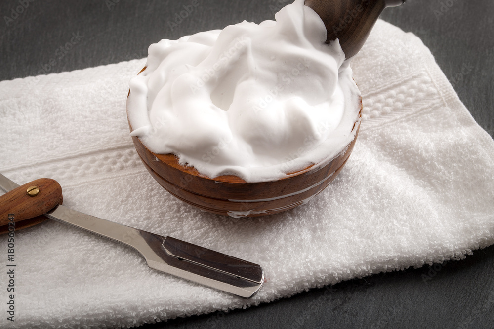 Male cosmetic products and supplies used by men to shave concept with a straight razor, towel, shaving brush and foam on dark grey background Male cosmetic products and supplies used by men to shave concept with a straight razor, towel, shaving brush and foam on dark grey background