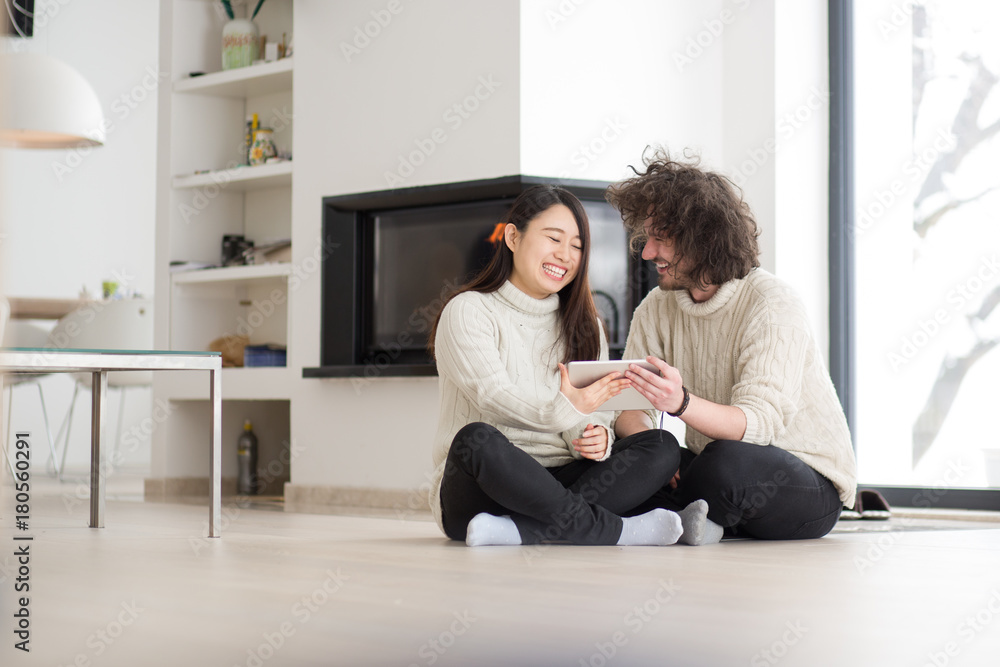 multiethnic couple using tablet computer in front of fireplace multiethnic couple using tablet computer in front of fireplace