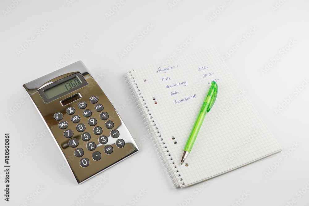 Ein Schreibblock mit einer Berechnung der Ausgaben, ein grüner Stift und Taschenrechner Ein Schreibblock mit einer Berechnung der Ausgaben, ein grüner Stift und Taschenrechner