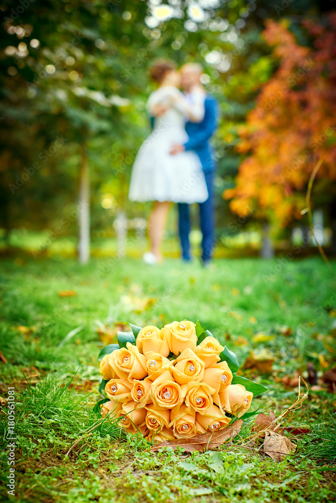 wedding bouquet lying on a green grass in the foreground, blurred background,  against the background of the bride and groom kissing, wedding, wedding  walk, autumn wedding Stock Photo | Adobe Stock