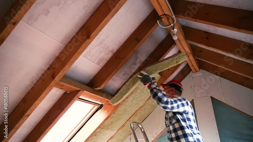 Man installing thermal roof insulation layer  - using mineral wool panels. Attic renovation and insulation concept