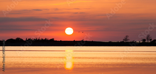 solnegång vid vatten solen speglas i det lugna havet siluett av land vid horisonten photo