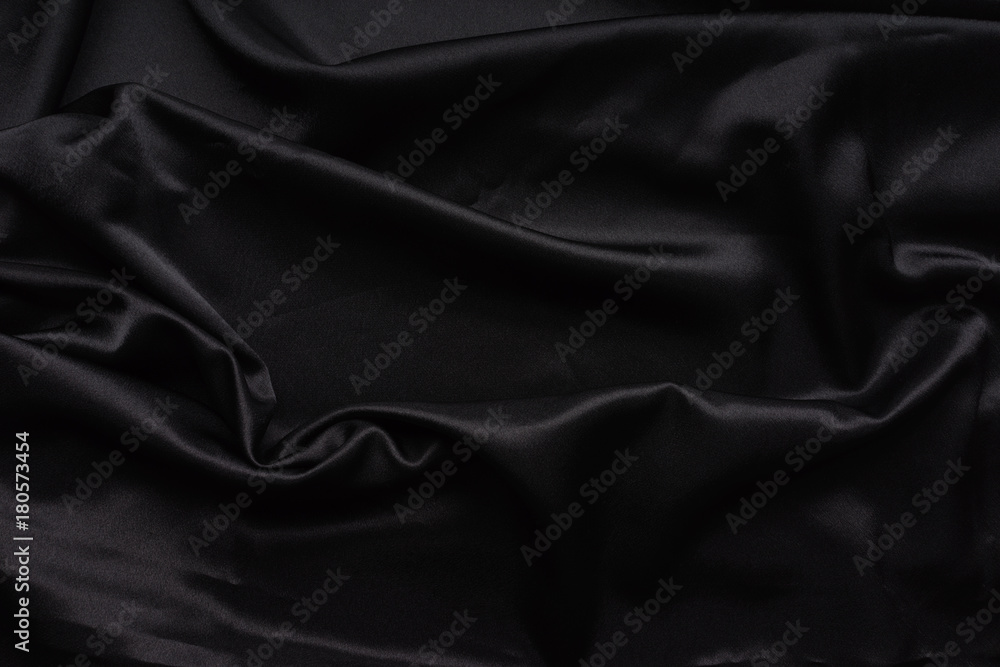 Dark black silky, satin  fabric, wave, draperies. Beautiful textile backdrop. Close-up. Top view 