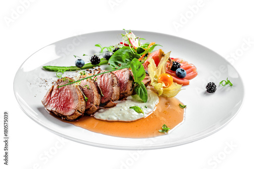 Delicious medium rare meat steak with sauce and salad on a plate. Healthy food made of meat fillet and fresh herbs isolated on a white background.