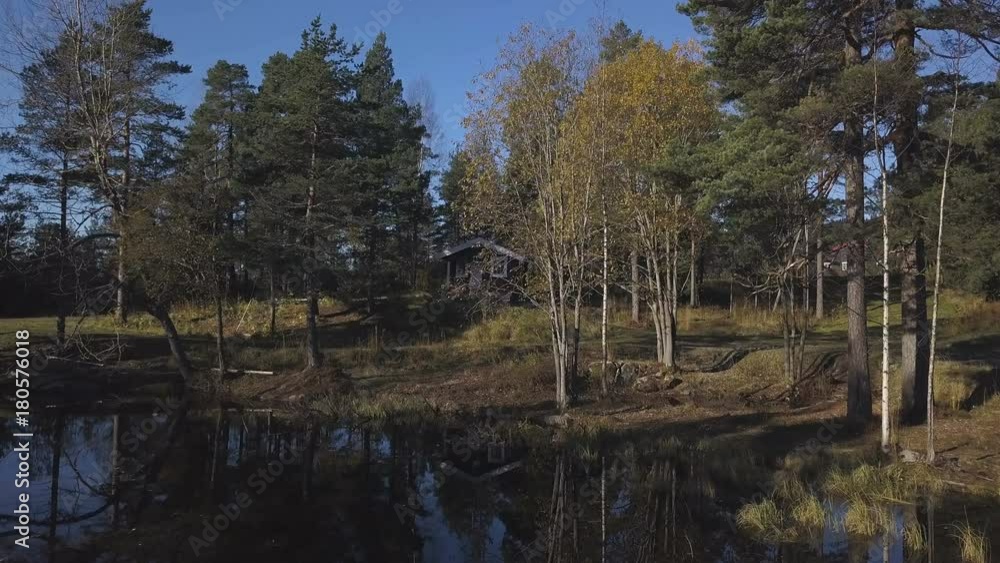 Small wooden house near the edge of a small river or pond amidst lush foliage, approaching the sunset. Small wooden house near the edge of a small river or pond amidst lush foliage, approaching the sunset.