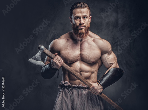 A man holds axe over dark grey background.