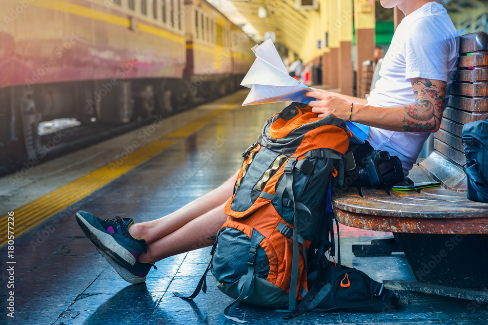 Fototapeta premium Man holding a map with backpack, camera and a smart phone in a train station