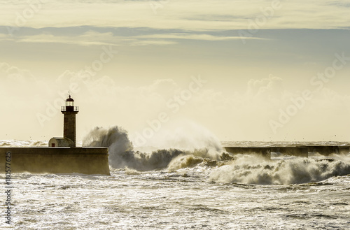Landscape seascape lighthouse battered by huge waves on Atlantic Ocean with blue green skies and puffy clouds. © Jim