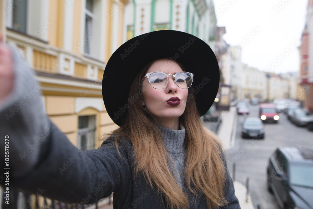 Stylish girl takes selfie street while walking around the beautiful city. Tourist hipster posing for the camera of your phone and make selfie. Stylish girl takes selfie street while walking around the beautiful city. Tourist hipster posing for the camera of your phone and make selfie.