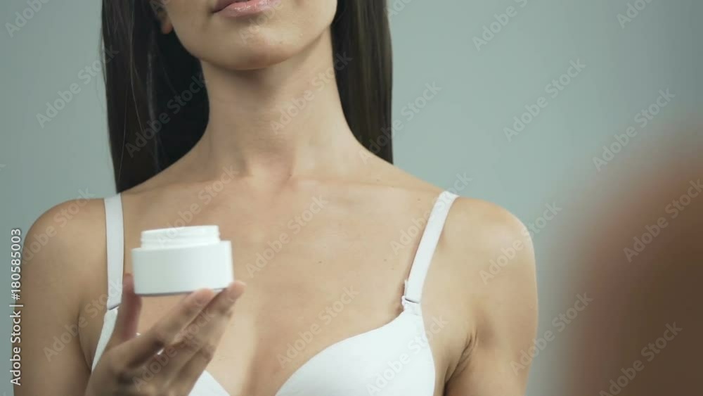 Young woman holding tub with face cream, opening and applying it, anti-aging Young woman holding tub with face cream, opening and applying it, anti-aging