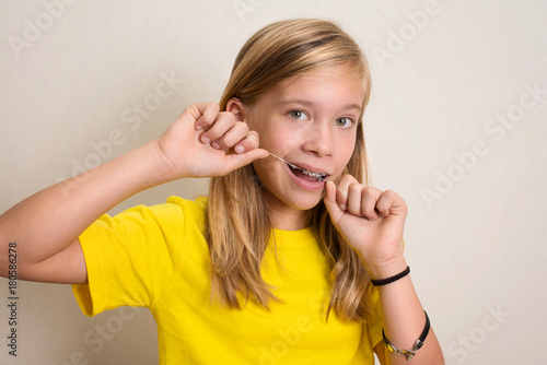 Girl with dental braces flossing teeth. Close-up portrait of pre teen girl with dental floss isolated.