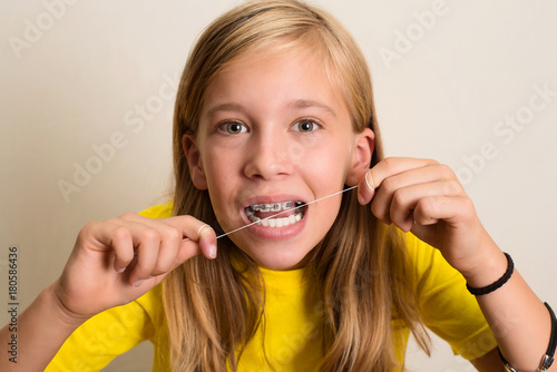Funny girl with dental braces flossing her teeth. Close-up portrait of pre teen girl with dental floss isolated.