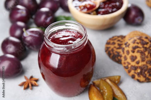 Glass jar with delicious plum jam on table