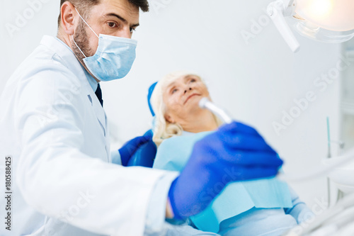 Love my job. Close up of skilled dentist holding medical instrument while preparing for examination and standing near the patient