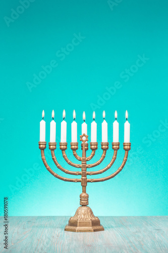 Bronze Hanukkah menorah with burning candles on wooden table front old vintage aquamarine wall background. Holiday greeting card concept. Retro style filtered photo