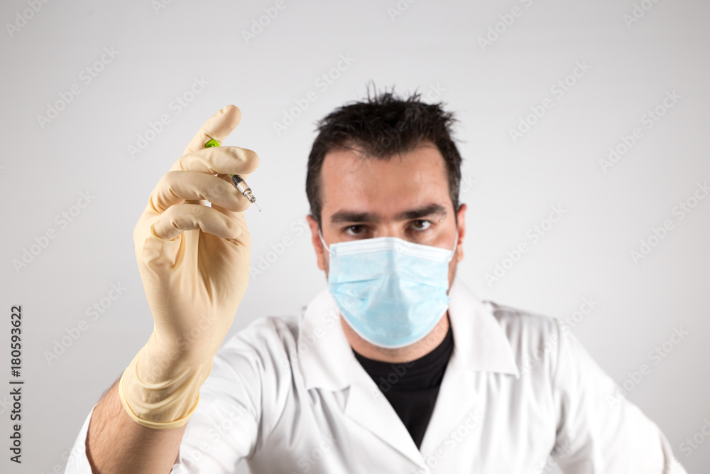 Doctor with syringe ready to give a vaccine injection. Young man in doctor outfit with a syringe, looking threatening. Doctor with syringe ready to give a vaccine injection. Young man in doctor outfit with a syringe, looking threatening.