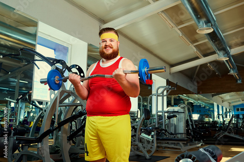 Thick man doing exercises with a barbell in the gym.