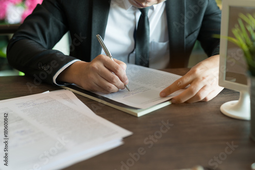 Business concept: Businessman sitting at coffee shop. is writing signs a contract. Holding pen in hand photo