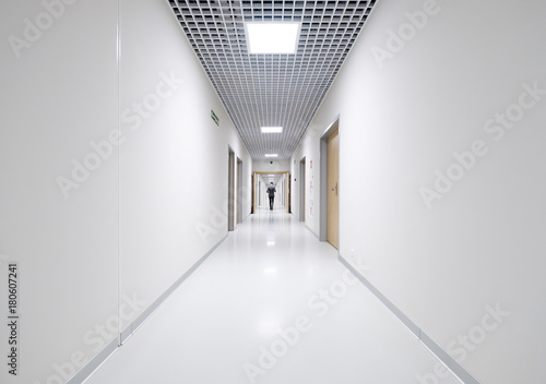 Valokuvatapetti Business man back view at long white empty corridor interior