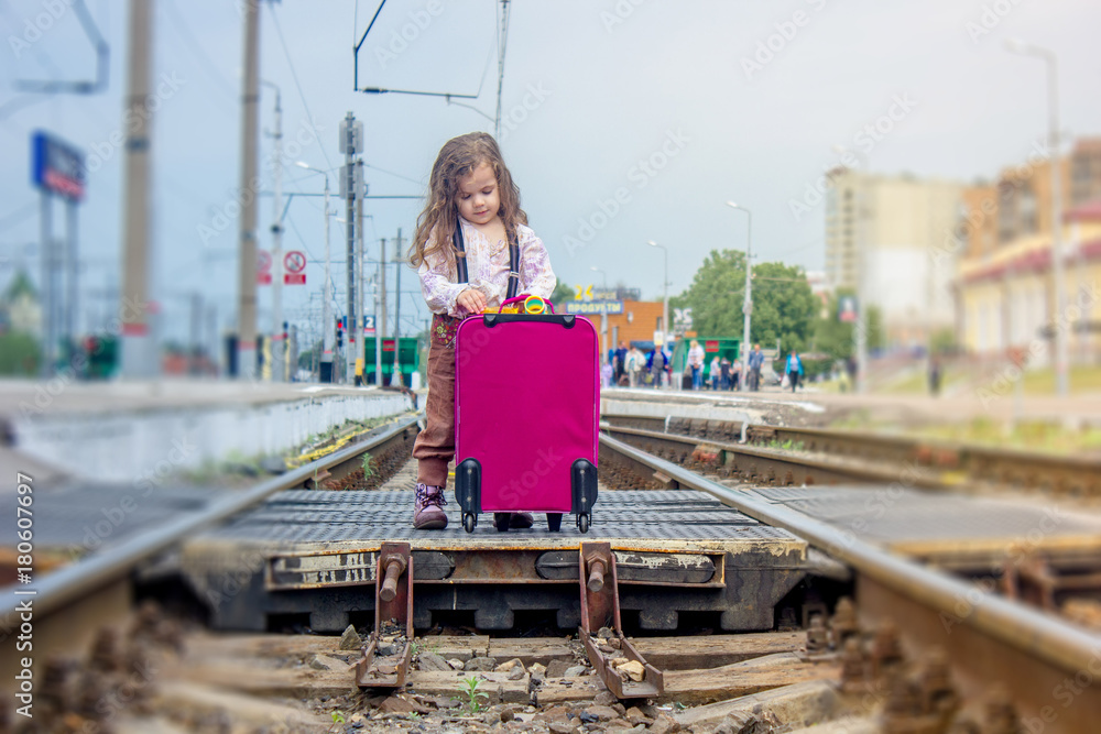 Little girl stay on the rails on railway station.