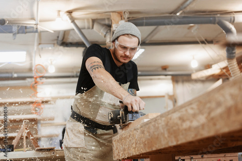 Obraz na plátně Carpenter working with electric planer on wooden plank in workshop