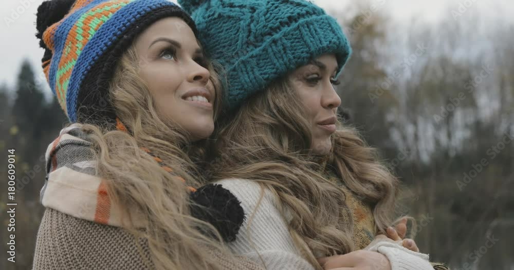close up, beautiful sisters warming up and enjoying the view on nature, wearing sweater, hat or beanie, smiling close up, beautiful sisters warming up and enjoying the view on nature, wearing sweater, hat or beanie, smiling