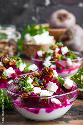 Vegetarian salad with baked beet, Greek yogurt, fresh parsley, walnuts and feta cheese in small glass bowls on the rustic wooden table.