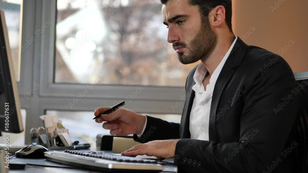 Happy young businessman excited for good news he received at the computer, sitting at desk in his office working with computer Happy young businessman excited for good news he received at the computer, sitting at desk in his office working with computer