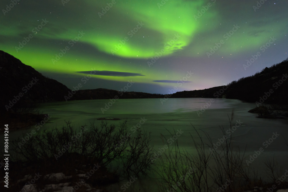 The Aurora in the night sky over hills and a frozen lake.