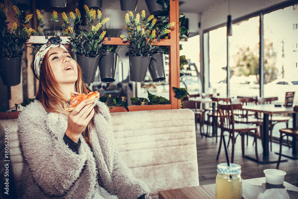 Happy young woman laughing while eating a slice of pizza