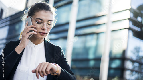 Businesswoman talking mobile phone and looking at watch in the outdoors