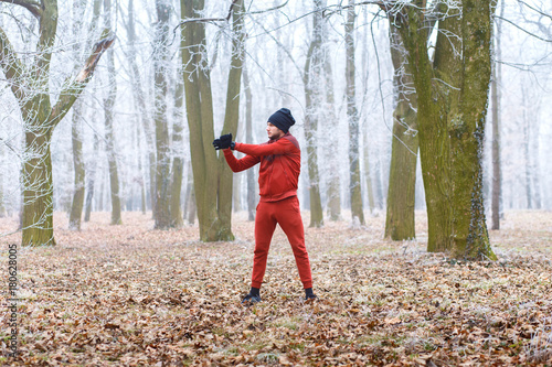 Young man stretching his muscles on a cold winter day before running in forest.