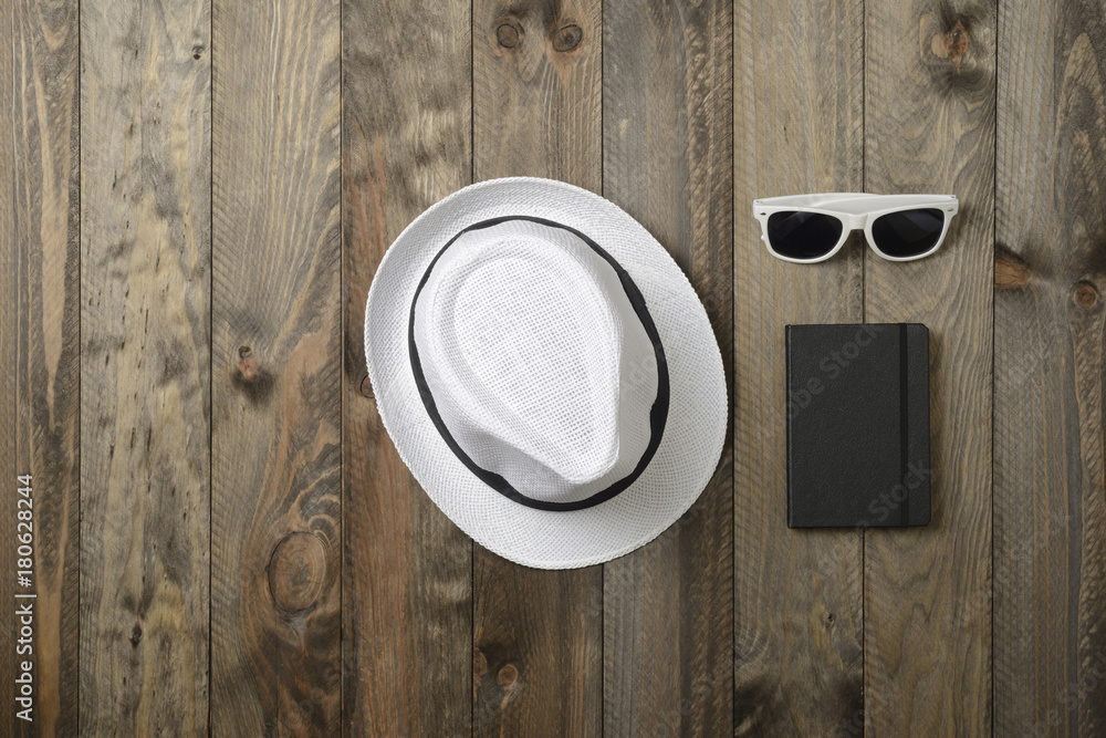 Sombrero blanco, gafas de sol y libreta sobre fondo de madera, vistos desde arriba Sombrero blanco, gafas de sol y libreta sobre fondo de madera, vistos desde arriba